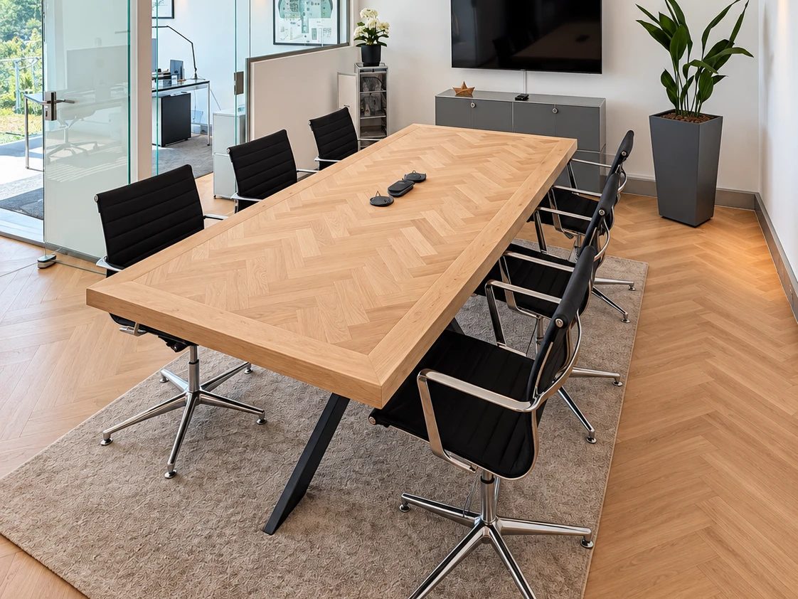 Besprechungsraum im Venit-Büro: Holztisch im Fischgrätmuster, schwarze Stühle, Glaswand zu den Büros