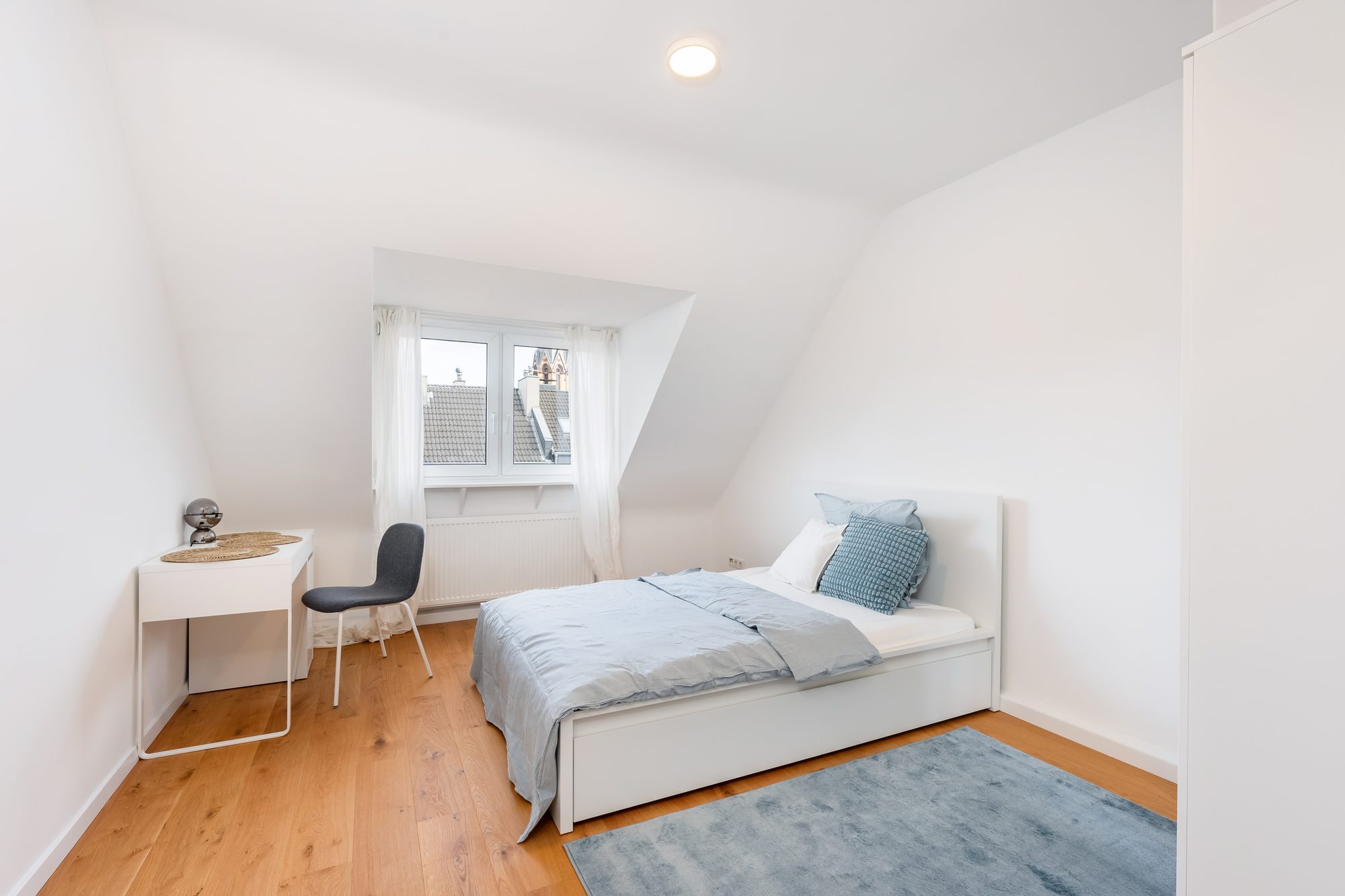 Möbliertes Zimmer mit Bett, Schreibtisch und Gaubenfenster